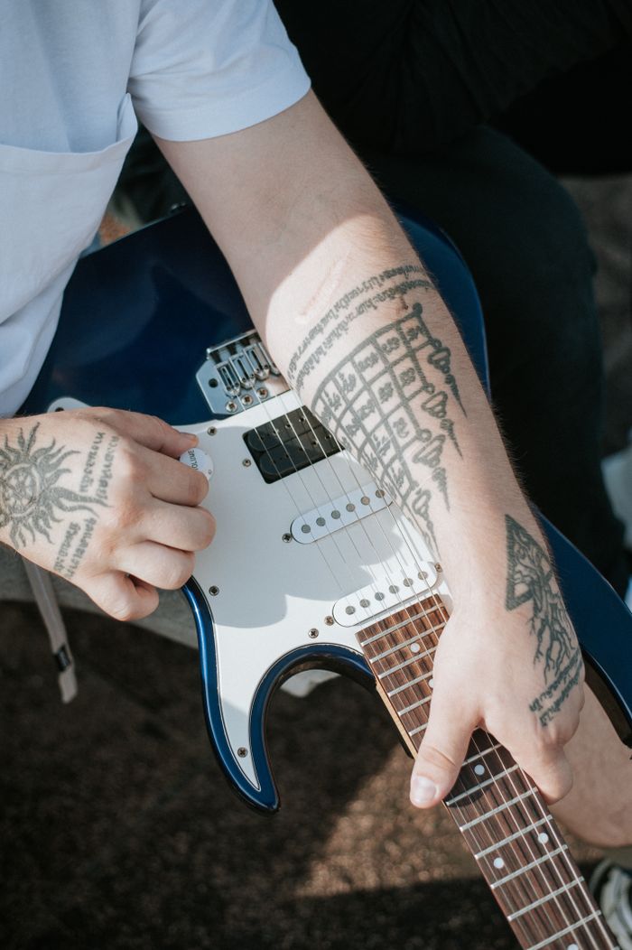 A close-up of tattooed hands holding a blue electric guitar, showcasing arm tattoos and music passion.