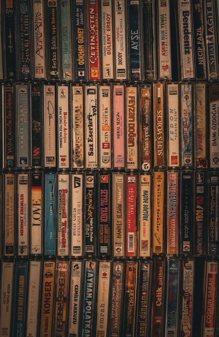 A nostalgic display of various cassette tapes showcasing diverse music genres on a vintage wooden shelf.