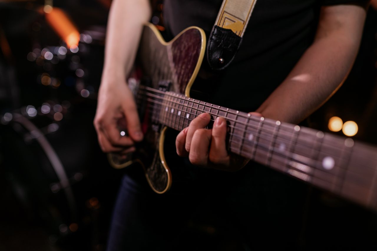 Musician strumming an electric guitar during live performance, emphasizing the strings and hands.